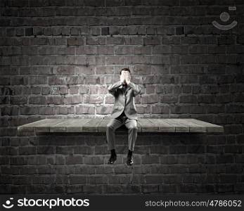Shocked businessman. Young shocked businessman sitting on stone and covering eyes with palms