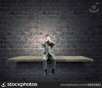 Shocked businessman. Young shocked businessman sitting on stone and covering eyes with palms
