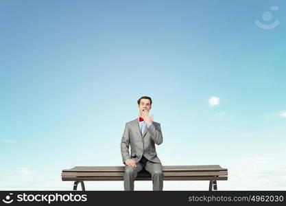 Shocked businessman. Young shocked businessman sitting on wooden bench