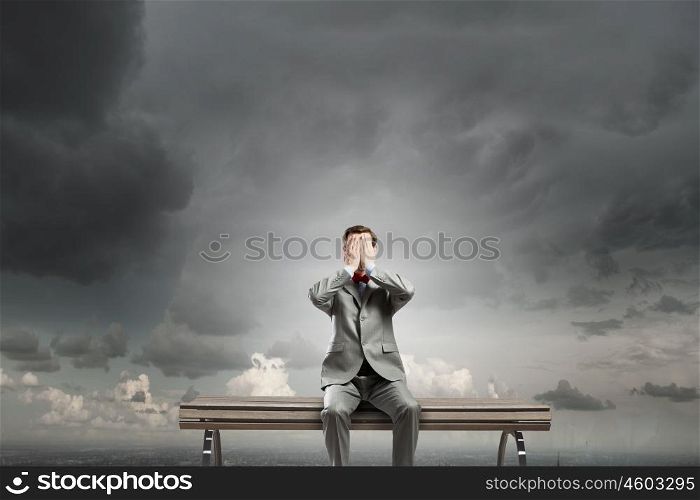 Shocked businessman. Young shocked businessman sitting on wooden bench and covering eyes with palms