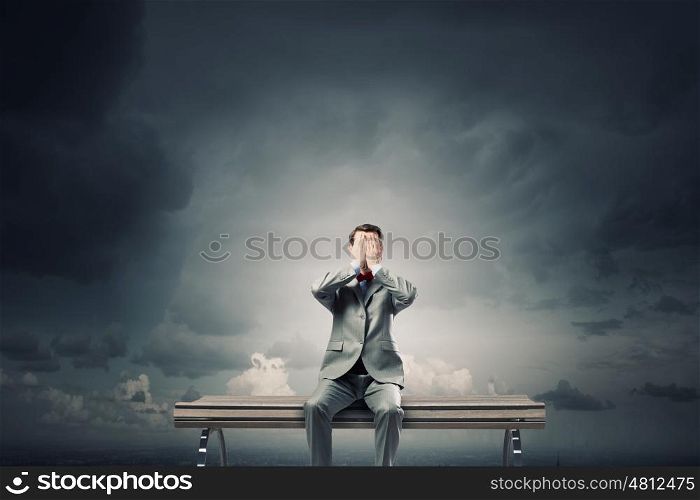 Shocked businessman. Young shocked businessman sitting on wooden bench and covering eyes with palms