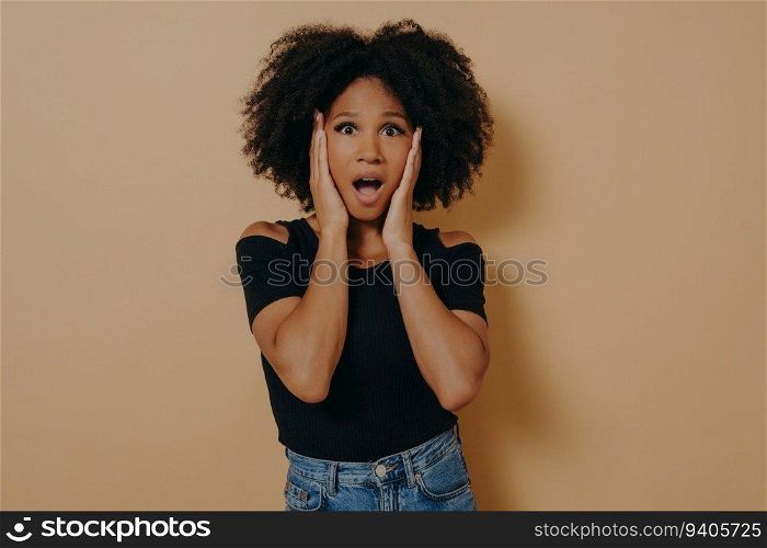 Shocked dark-skinned lady in trendy black t-shirt, hands on cheekbones, disbelief over low price discount. Studio shot