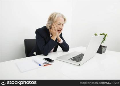 Shocked senior businesswoman using laptop at desk in office