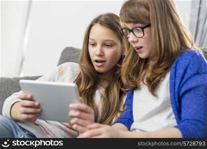 Shocked sisters using digital tablet on sofa at home