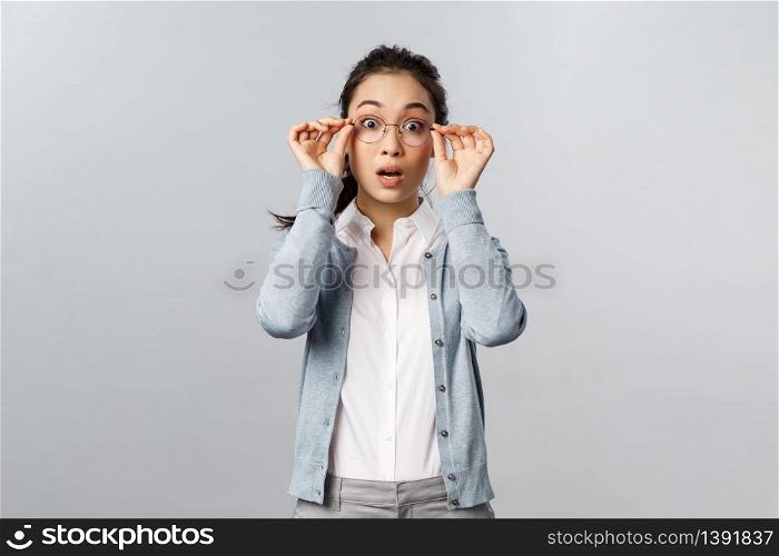 Shocked, startled attractive asian woman staring in awe, drop jaw and gasping, put on glasses to see fascinating piece of art at exhibition, staring impressed and wondered, grey background.. Shocked, startled attractive asian woman staring in awe, drop jaw and gasping, put on glasses to see fascinating piece of art at exhibition, staring impressed and wondered, grey background