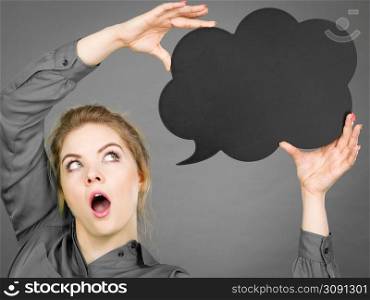 Shocked student looking woman wearing grey shirt holding black thinking bubble, gray background.. Shocked woman holding black thinking bubble