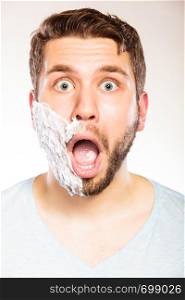 Shocked surprised young man with shaving cream foam on half of face beard. Handsome guy preparing to shave. Skin care and hygiene.. Shocked man with shaving cream foam on half face.