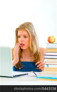 Shocked teen girl sitting at table with books and looking on laptop &#xA;
