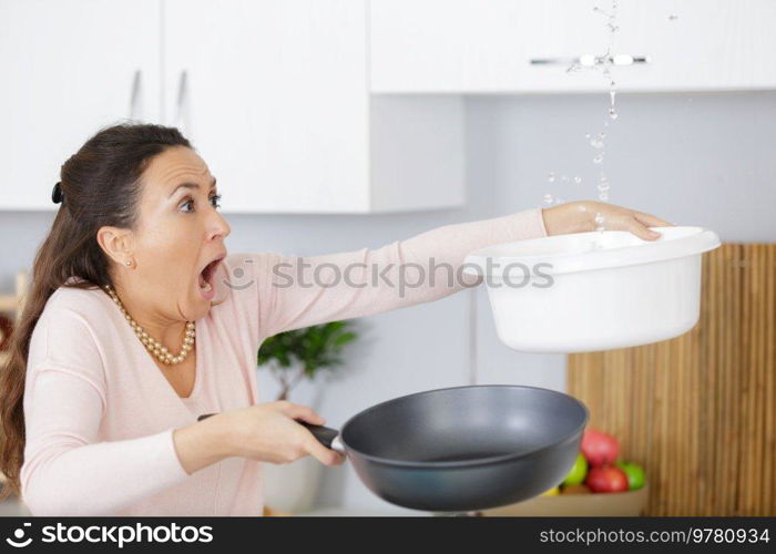 shocked woman calling collecting water leaking from ceiling