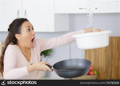 shocked woman collecting water leaking from ceiling using utensil