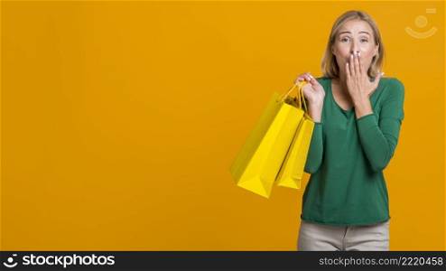 shocked woman covering her mouth while holding many shopping bags with copy space