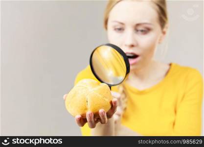 Shocked woman holding bun bread roll and magnifying glass examine wheat product ingredients seeing something disgusting. Shocked woman magnifying bun bread roll