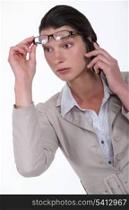 Shocked woman lifting glasses during call