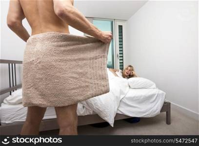 Shocked woman looking at nude man holding towel in bedroom