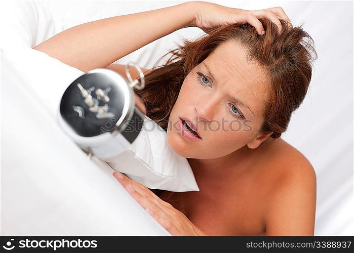 Shocked woman watching alarm clock in white bed