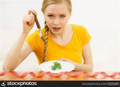 Shocked young blonde woman dealing with anorexia nervosa or builimia having small green vegetable on plate. Dieting problems, eating disorder.. Shocked young woman being on diet