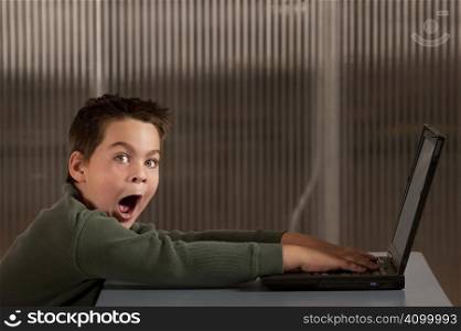 Shocked young boy reacting to info on a laptop computer