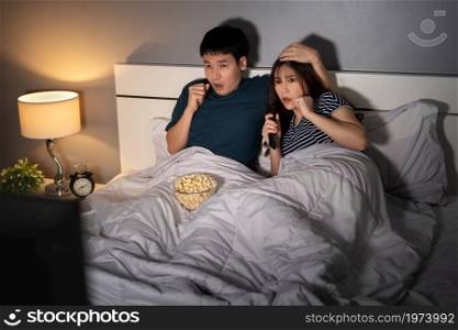 shocked young couple watching TV movie on a bed at night