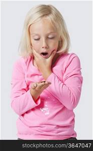 Shocked young girl holding coins over white background