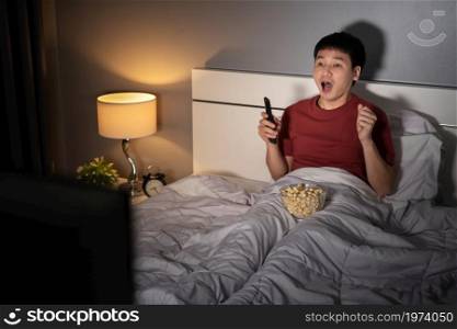 shocked young man watching TV movie on a bed at night