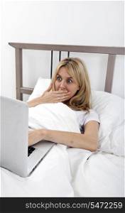 Shocked young woman looking at laptop in bed