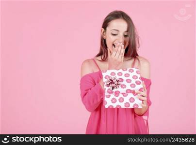 shocked young woman opening floral present box with bow against pink background