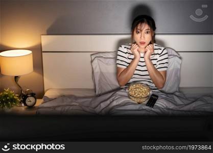 shocked young woman watching TV movie on a bed at night