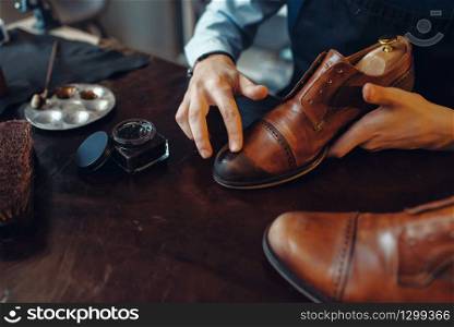 Shoemaker applies black shoe polish, footwear repair service. Craftsman skill, shoemaking workshop, master works with boots, cobbler shop