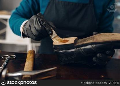 Shoemaker smears glue to the shoe, footwear repair service. Craftsman skill, shoemaking workshop, master works with boots, cobbler job