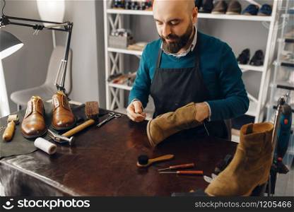 Shoemaker stitches the shoe, footwear repair service. Craftsman skill, shoemaking workshop, master works with boots. Shoemaker stitches the shoe, footwear repair