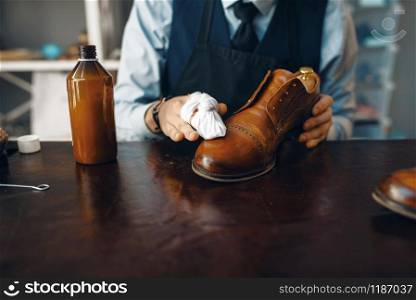 Shoemaker wipes black shoe polish, footwear repair service. Craftsman skill, shoemaking workshop, master works with boots, cobbler shop. Shoemaker wipes black shoe polish, footwear repair