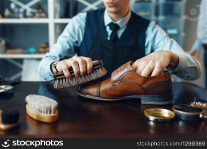 Shoemaker wipes black shoe polish, footwear repair service. Craftsman skill, shoemaking workshop, master works with boots, cobbler shop