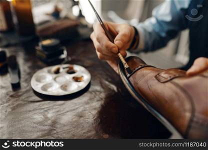 Shoemaker with brush tints shoes, footwear repair service. Craftsman skill, shoemaking workshop, master works with boots, cobbler. Shoemaker with brush tints shoes, footwear repair
