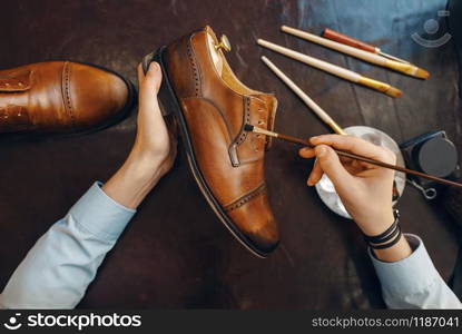 Shoemaker with brush tints shoes, footwear repair service. Craftsman skill, shoemaking workshop, master works with boots, cobbler shop