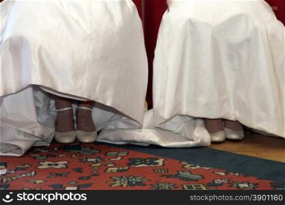 shoes and white dresses of two brides sitting next to each other