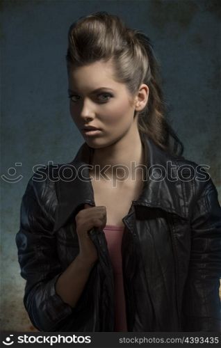 shoot of young fashion girl with wavy brunette hair-style posing with leather jacket in dark atmosphere