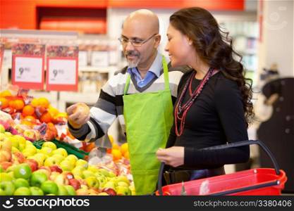 Shop assistant holding apple with customer in the supermarket