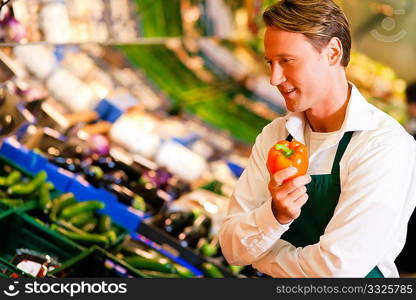 Shop assistant in a supermarket at the vegetable shelf inspecting the stuff for sale