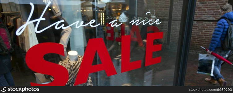 shop window with sale sign and passing man with umbrella and bag