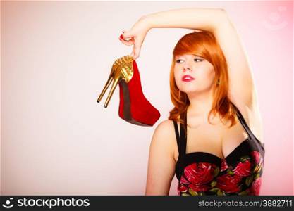 Shopaholic, fashion and women style. Shopping time. Young red haired female holding high heeled shoes in hands on pink background. Studio shot.