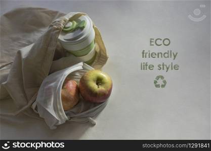 Shopper bag with collapsible silicone mug and apples in mesh bag in the sunlight with shadows. Zero waste concept. Chalk inscription ECO friendly life style and recycling symbol