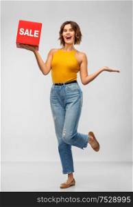 shopping and people concept - happy smiling young woman in mustard yellow top and jeans with sale sign posing over grey background. happy smiling young woman posing with sale sign
