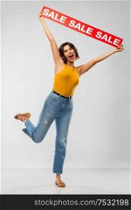 shopping and people concept - happy smiling young woman in mustard yellow top and jeans with sale banner posing over grey background. happy smiling young woman posing with sale banner