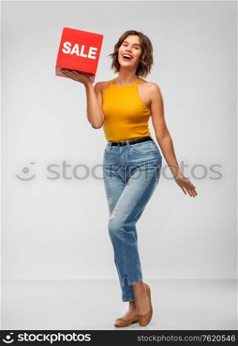 shopping and people concept - happy smiling young woman in mustard yellow top and jeans with sale sign posing over grey background. happy smiling young woman posing with sale sign
