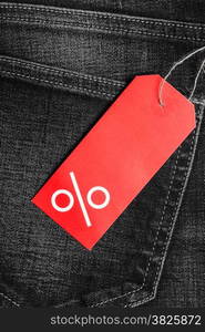 Shopping and sale concept. Closeup red label with percent sign and copy space on black jeans pocket denim cotton material background