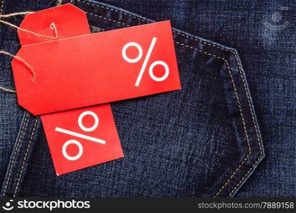 Shopping and sale concept. Closeup two red labels with percent sign and copy space on navy blue jeans pocket denim cotton material background