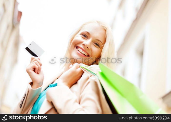 shopping and tourism - beautiful woman with shopping bags and plastic card in ctiy