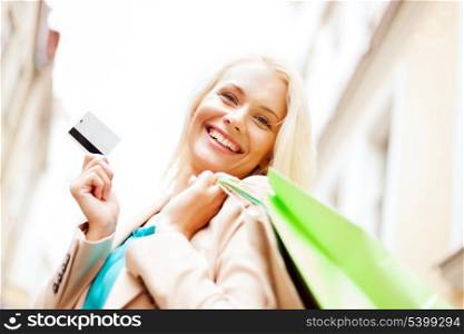 shopping and tourism - beautiful woman with shopping bags and plastic card in ctiy