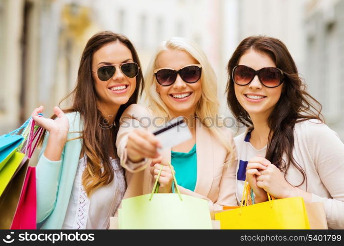 shopping and tourism concept - beautiful girls with shopping bags and credit card in ctiy