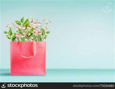 Shopping bag in living coral color with flowers bunch standing on table at turquoise wall background. Branding mock up. Copy space. Purchase , sale and promotion. Spring or summer banner or template.